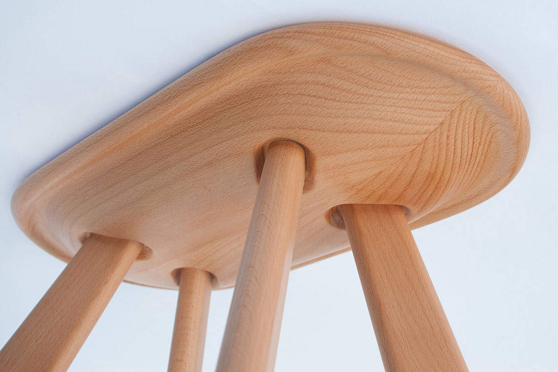 Atlas solid wood stool in beech wood is shown from underneath the seat showing leg insertion detail