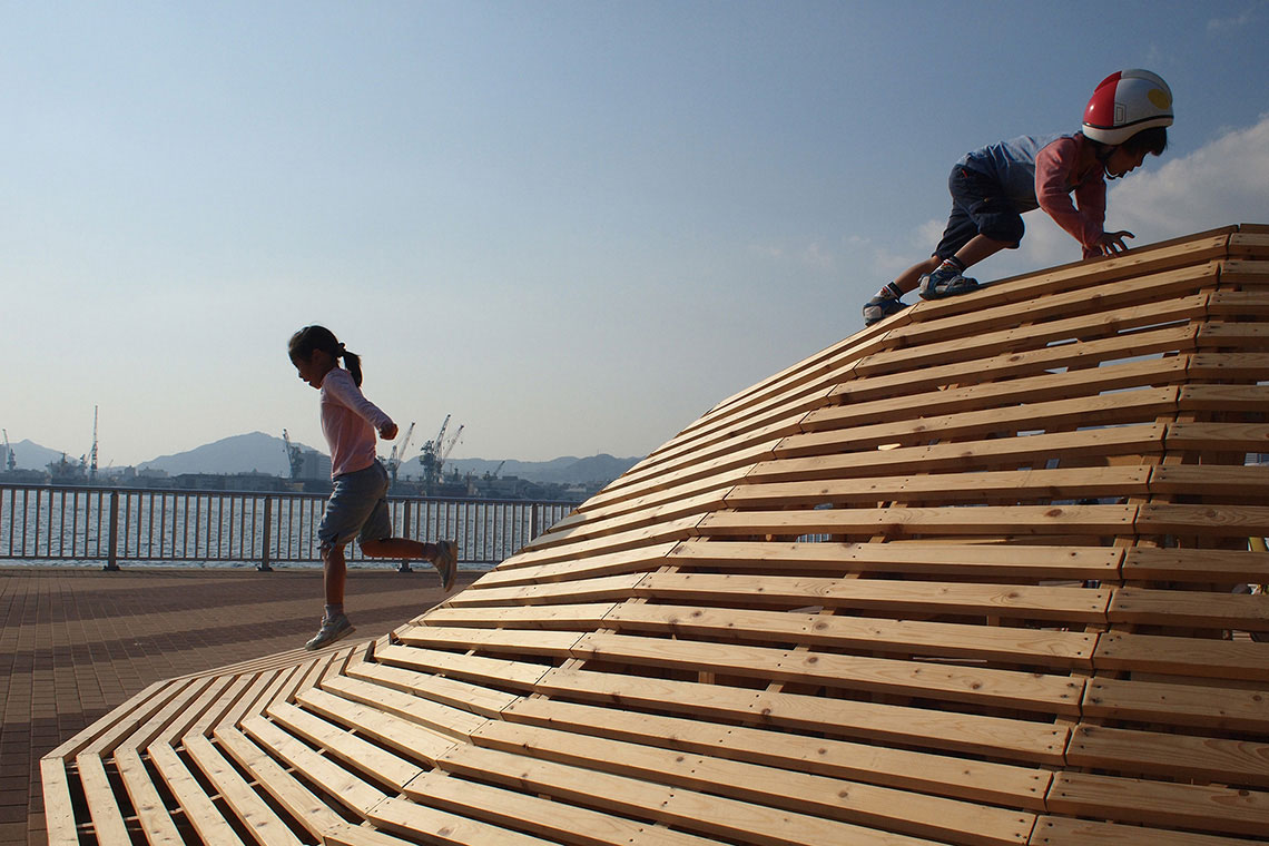Two kids are climbing Crater Lake installation, a wood mountain-scape situated in Shiosai Park in Kobe.