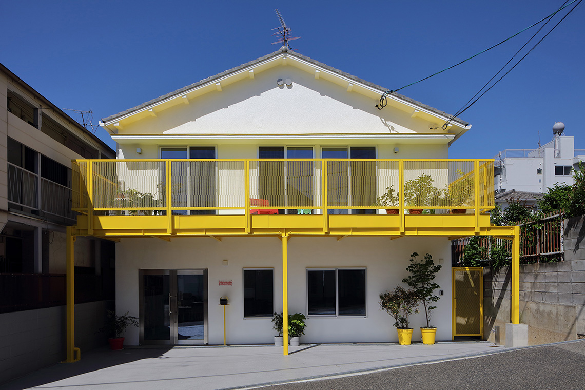 アーチだらけの家の正面ファサードは白地の壁と黄色いバルコニーが特徴