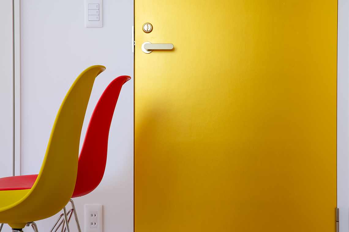Kitano House Renovation by 24d-studio large detail of gold door with yellow and red chairs in front of the door