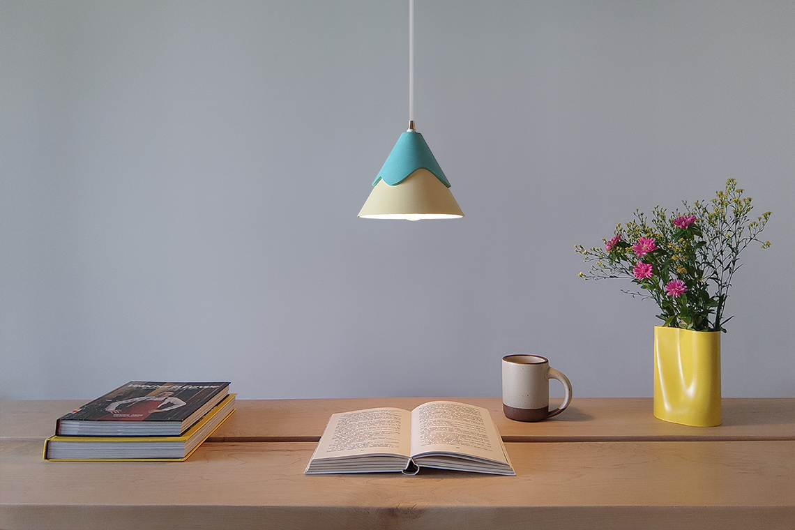 Rei Pendant light in green and yellow hues is suspended over a dining table creating a warm and serene atmosphere.